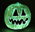 A glowing green jack-o’-lantern with triangular eyes and a toothy, zigzag mouth, illuminated against a dark background.