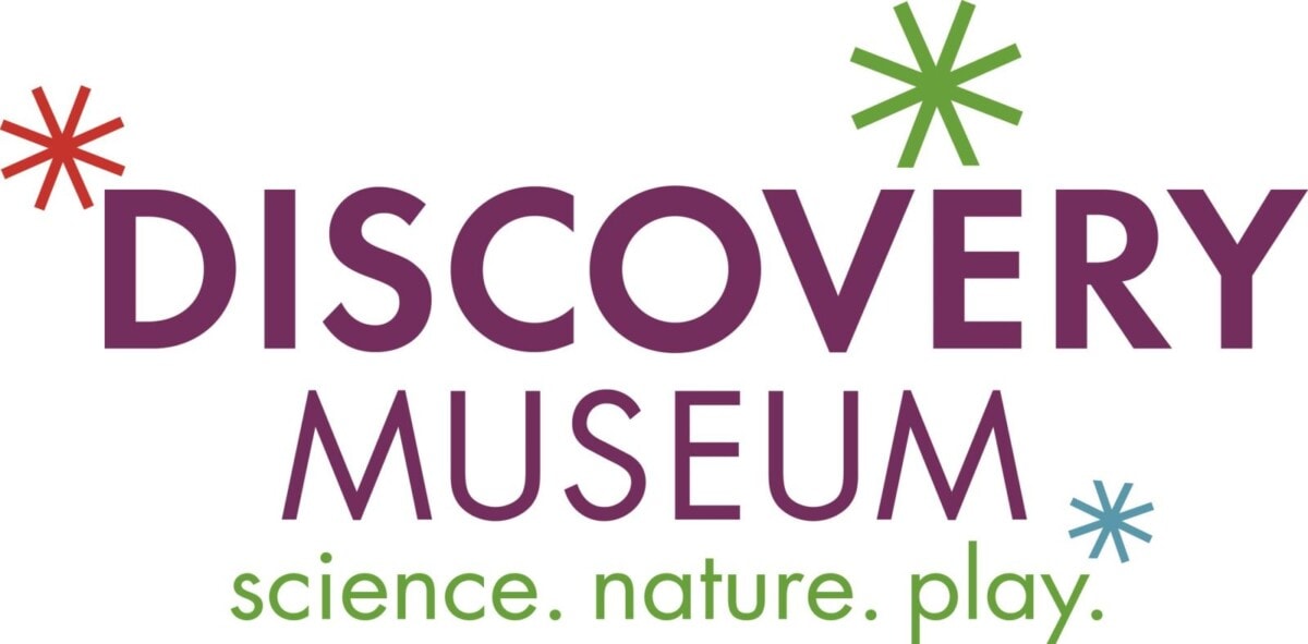 Logo for the Discovery Museum with colorful asterisks and the tagline “science. nature. play.” in green and purple text.
