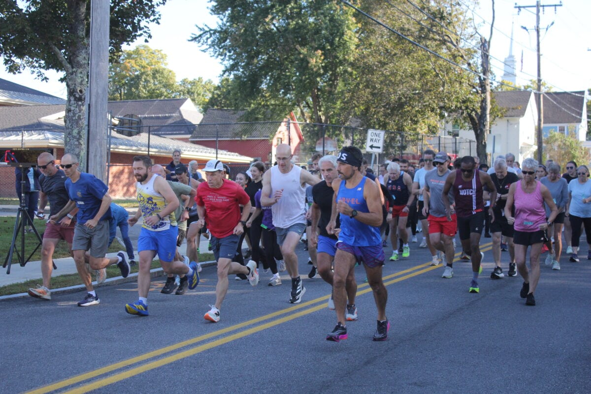Photograph of the runners at the start of the 2026 Hubbardston Public Library Road Race. Men and women running in a group on the road.